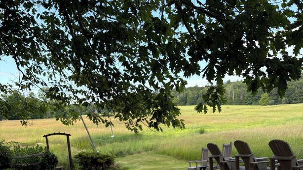 An outdoor dining table set with plates, glasses, and cutlery, surrounded by chairs, with a grassy field and trees in the background. - Historic 1789 Luxury Farmhouse near Dartmouth College (Hartford)