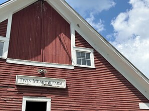 A red barn with a white trim and a sign that reads 'Twin Meadow Farm.'