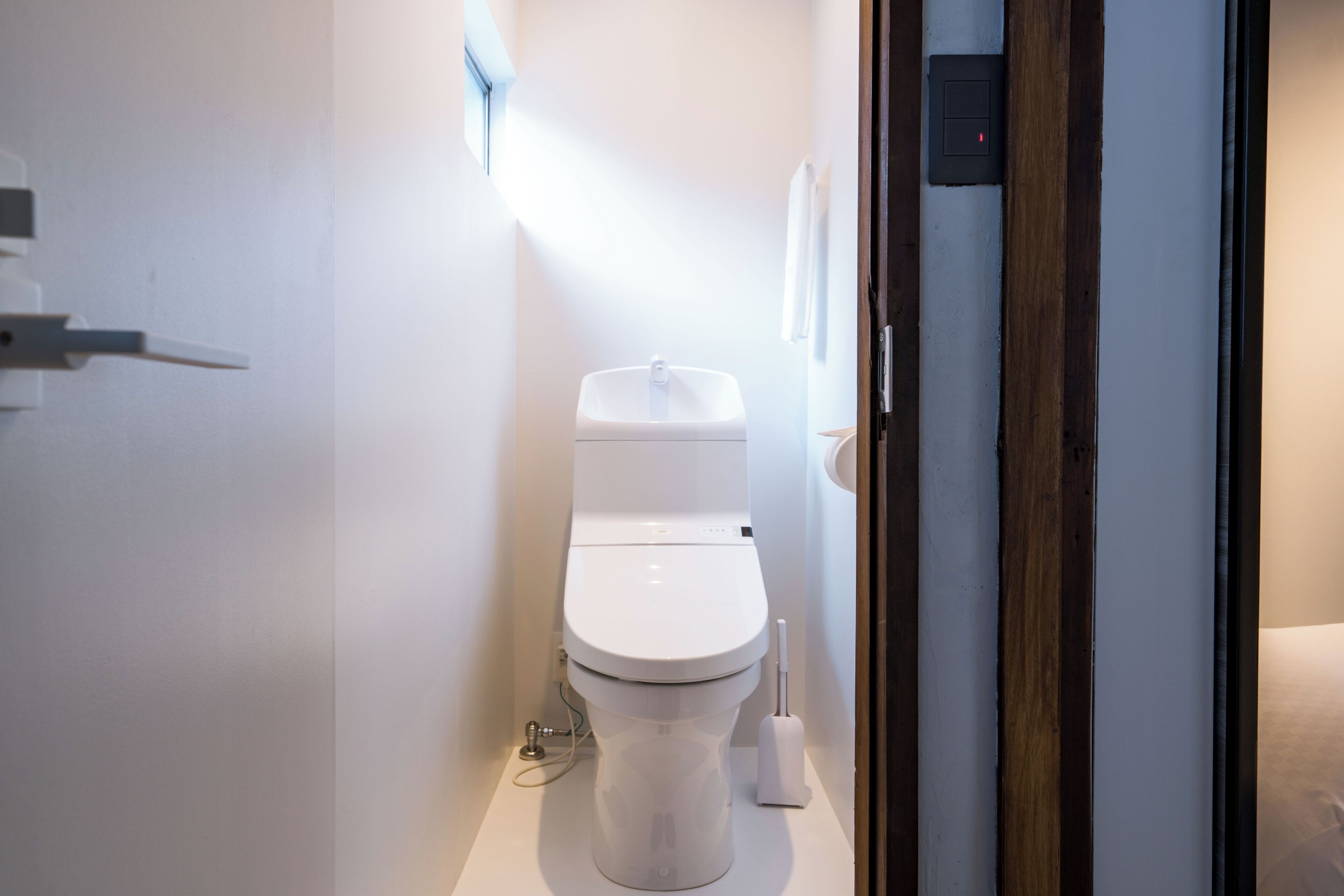 A modern bathroom with a white toilet, a hand dryer, and a wall-mounted light fixture.