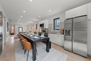 A modern kitchen with a long dining table, stainless steel appliances, and a large refrigerator. - Station580 | 8 min OSU | Hot Tub, Mini Golf, Games (Columbus)