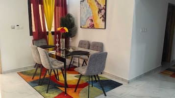 A dining area with a glass table and grey upholstered chairs, a colorful rug, and a painting on the wall.