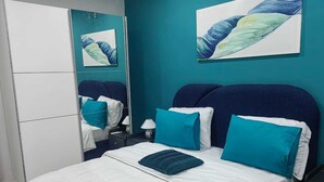 A bedroom with a bed, a nightstand, a mirror, and artwork on the wall. - 2-bedroom Residences meublees in soothing Bouake with AC comfort (Bouake)