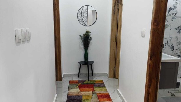 A hallway with a colorful rug, a round mirror on the wall, and a small table with a plant. - 2-bedroom Residences meublees in soothing Bouake with AC comfort (Bouake)