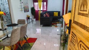 A modern living room with a sofa, chairs, a glass dining table, and a colorful rug. - 2-bedroom Residences meublees in soothing Bouake with AC comfort (Bouake)