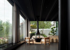 Ein modernes Interieur mit großen Fenstern, einer zentralen schwarzen Pendelleuchte und einer Sitzecke mit rundem Tisch.