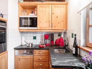 A kitchen with wooden cabinets, a microwave, a coffee maker, and a wine bottle. - Franzosenstüberl - Uriger Troadkasten by Interhome (Rennweg am Katschberg)