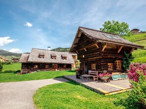 Eine Holzhütte mit Veranda, ein Rasenwagen mit Blumen und eine Bank.