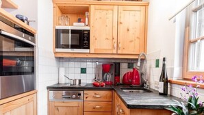 A compact kitchen with wooden cabinets, a microwave, a dishwasher, and a sink. - Franzosenstüberl - Uriger Troadkasten by Interhome (Rennweg am Katschberg)