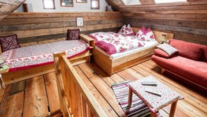 A loft bedroom with a sloped ceiling, wooden beams, a bed with floral bedding, a red sofa, and a small table with a remote control. - Franzosenstüberl - Uriger Troadkasten by Interhome (Rennweg am Katschberg)