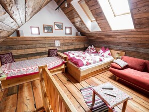 Ein Schlafzimmer im Loft-Stil mit schrägverdeckter Decke, Holzbalken, einem Bett mit floraler Bettwäsche, einem roten Sofa und einem kleinen Tisch mit Fernbedienung.