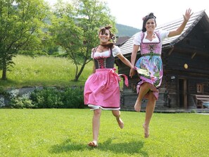 Two individuals in traditional attire running on a grassy field with a wooden building in the background. - Franzosenstüberl - Uriger Troadkasten by Interhome (Rennweg am Katschberg)