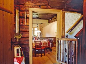 A rustic wooden interior with a dining area featuring a table and chairs, a wooden staircase, and a cross on the wall.