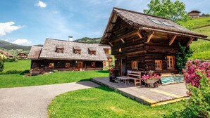 A wooden cabin with a porch, a wheelbarrow with flowers, and a bench. - Napoleonvilla - Ferienhaus für kreative Auszeiten by Interhome (Rennweg am Katschberg)