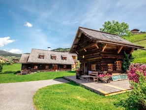 A wooden cabin with a porch, a wheelbarrow with flowers, and a bench. - Napoleonvilla - Ferienhaus für kreative Auszeiten by Interhome (Rennweg am Katschberg)