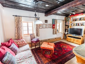 A cozy living room with a sofa, a wooden table, a bookshelf, and a television. - Napoleonvilla - Ferienhaus für kreative Auszeiten by Interhome (Rennweg am Katschberg)