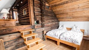 A log cabin interior with a wooden staircase, a bed with floral bedding, and a small table with a lamp. - Napoleonvilla - Ferienhaus für kreative Auszeiten by Interhome (Rennweg am Katschberg)