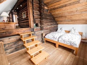 A log cabin interior with a wooden staircase, a bed with floral bedding, and a small table with a lamp. - Napoleonvilla - Ferienhaus für kreative Auszeiten by Interhome (Rennweg am Katschberg)