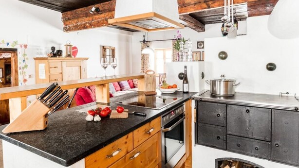 A kitchen with a black countertop, wooden cabinets, and a stove. - Napoleonvilla - Ferienhaus für kreative Auszeiten by Interhome (Rennweg am Katschberg)