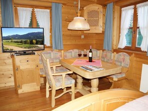 L’intérieur d’un chalet en bois, avec un téléviseur, une table à manger, des chaises et une bouteille de vin.