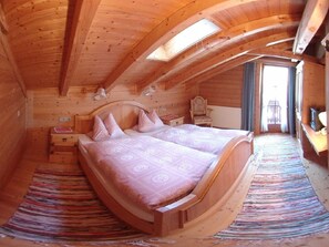 Ein gemütliches Schlafzimmer mit Holzbalkendecke, einem Bett mit gemusterten Textilien, einem Nachttisch und einem Sessel.