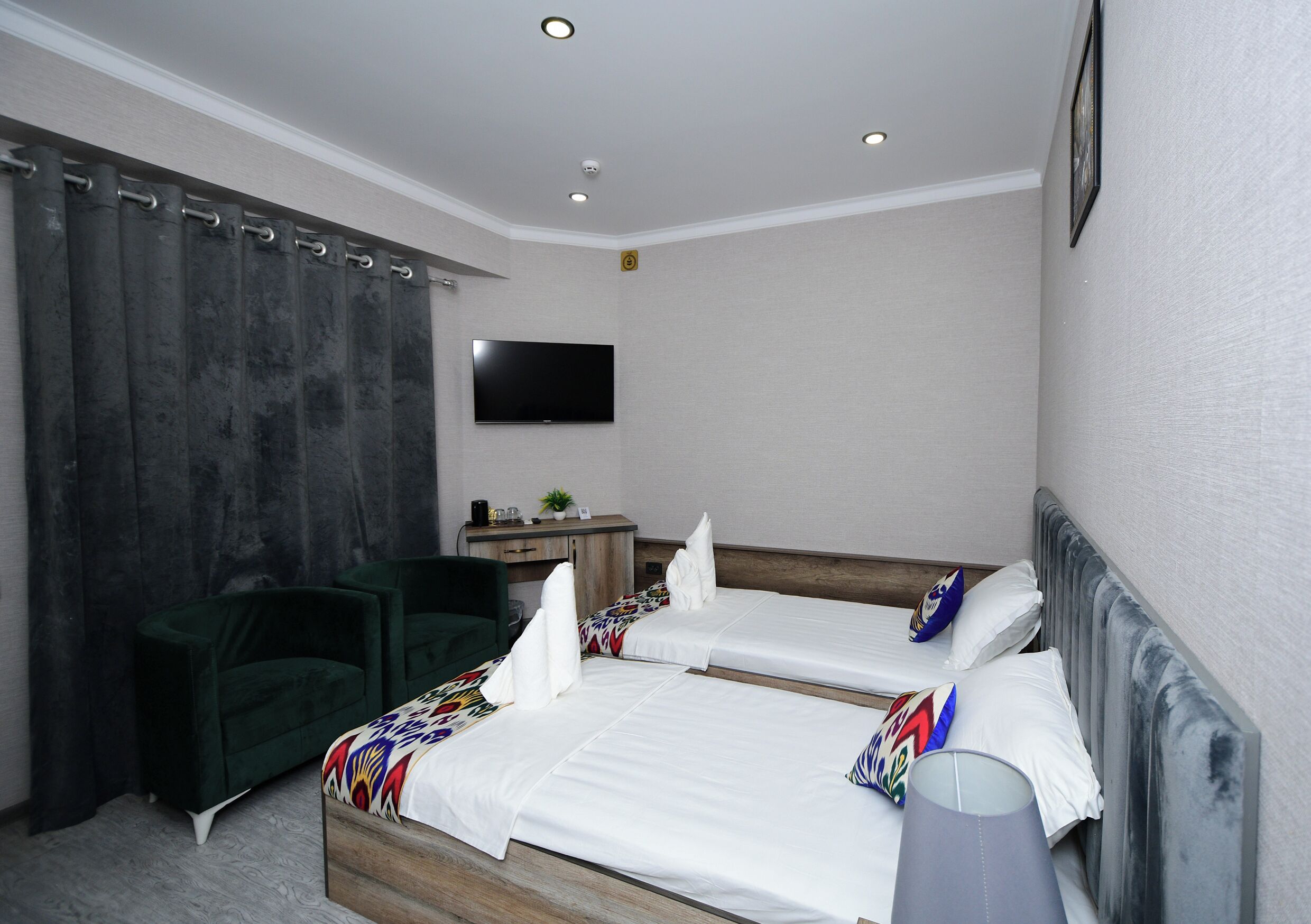 A hotel room with two beds, a desk, a chair, a TV, and a window with curtains.