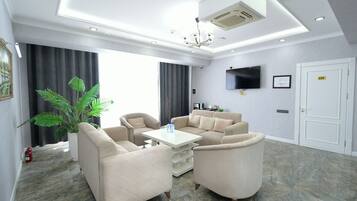 A modern living room with a sofa set, a coffee table, a flat-screen TV, and a large window with curtains.