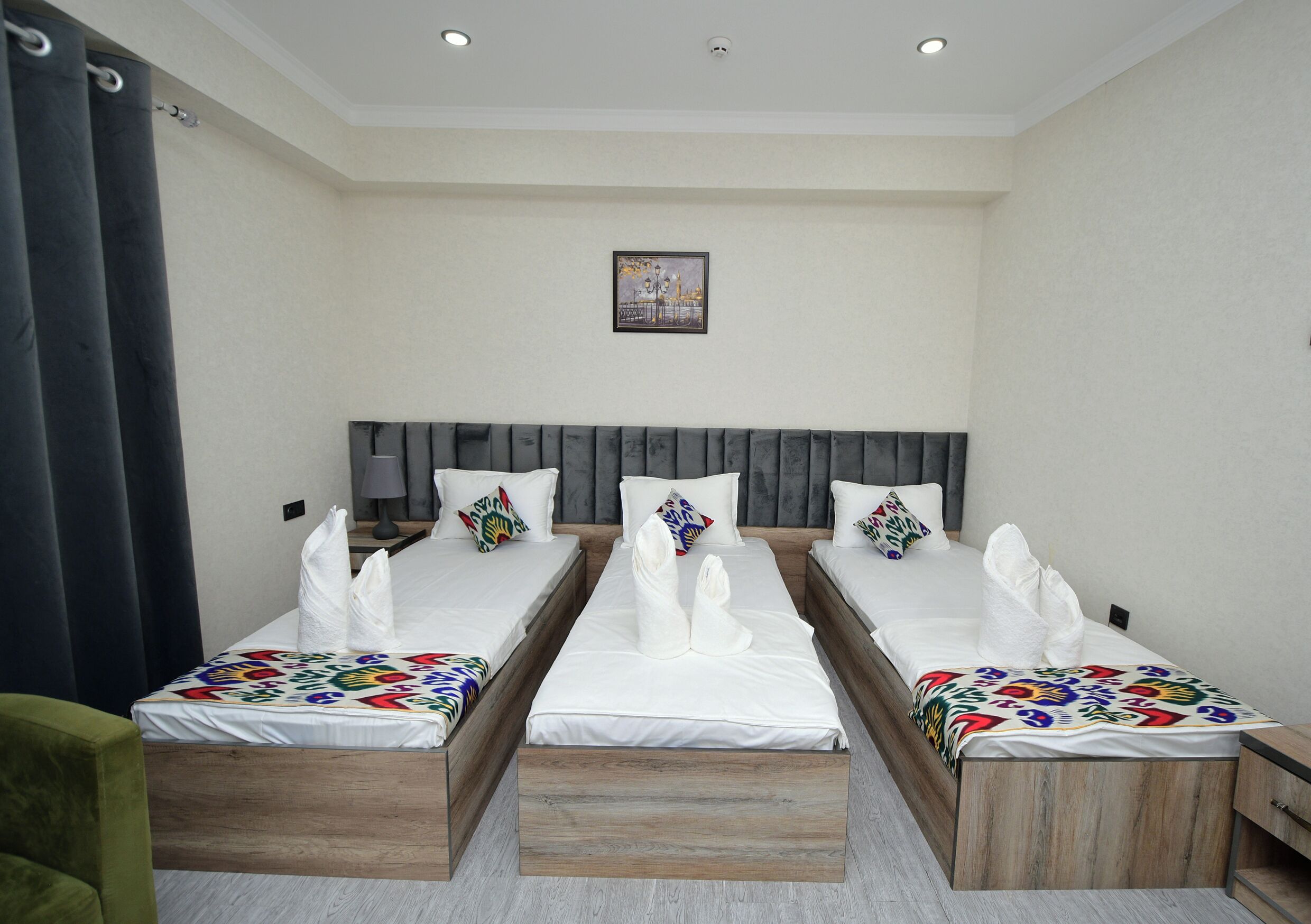 A hotel room with three single beds, a grey headboard, a framed picture on the wall, and a green chair.