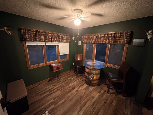 Una habitación con suelo de madera, ventilador de techo y ventanas con cortinas escocesas.
