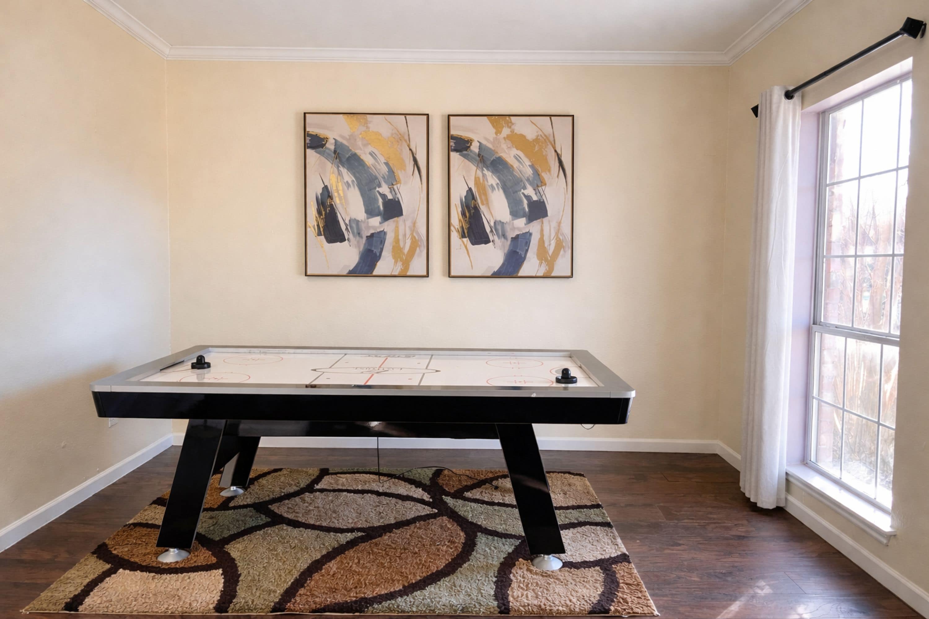 Een kamer met een tafelvoetbaltafel, twee abstracte schilderijen aan de muur en een groot raam.