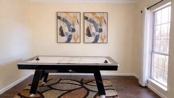 A room with a foosball table, two abstract paintings on the wall, and a large window.