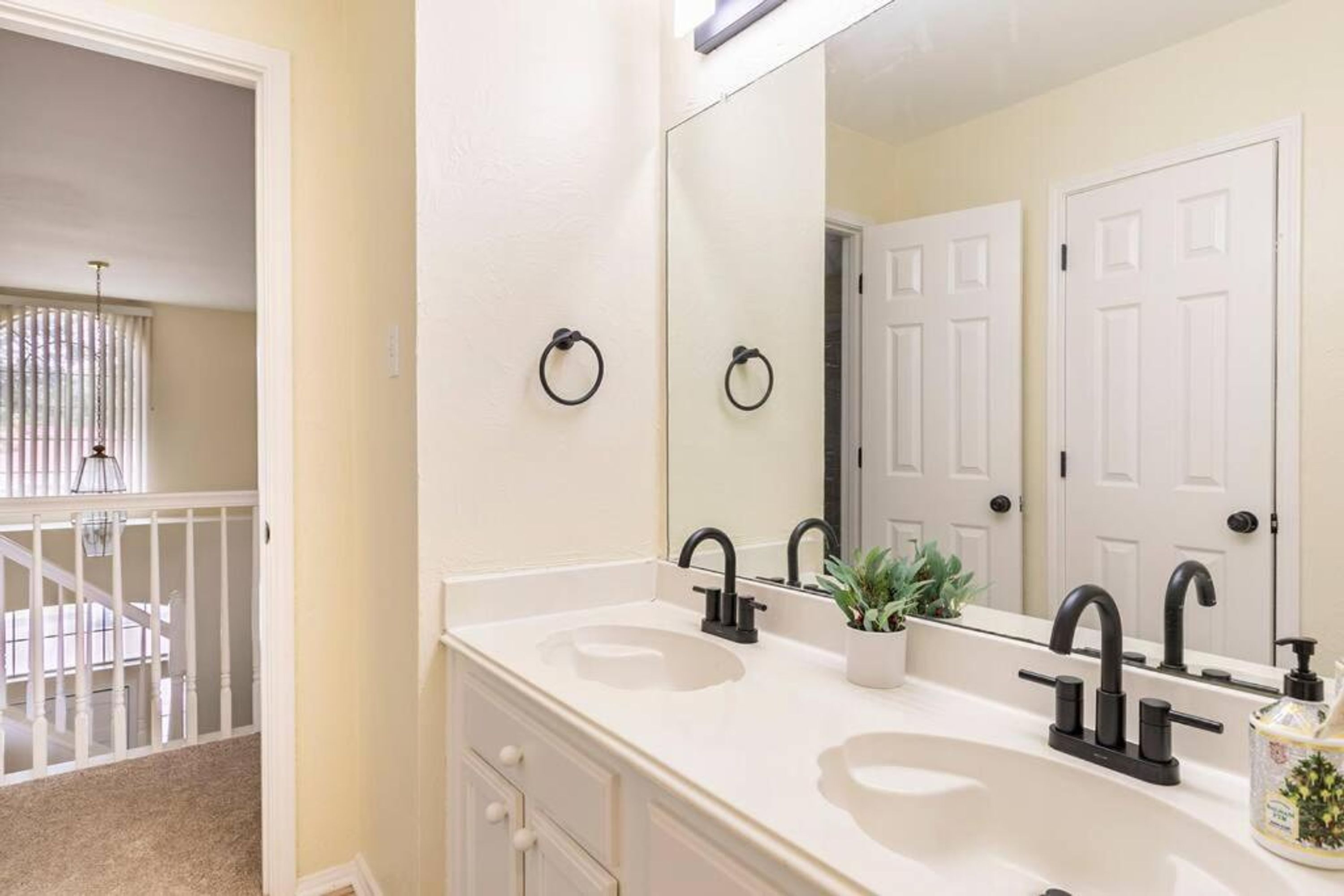 A bathroom with two sinks, a large mirror, and a door with a towel ring.