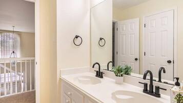 A bathroom with two sinks, a large mirror, and a door with a towel ring.