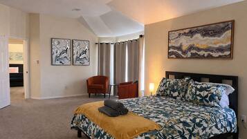 A bedroom with a bed, a chair, a painting, and a door leading to another room.