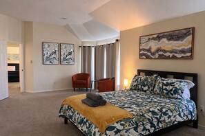 Un dormitorio con una cama, una silla, un cuadro y una puerta que da a otra habitación.