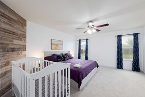 A bedroom with a crib, a bed with purple bedding, a ceiling fan, and a window with curtains. - Kitchen Foosball Fenced Yard Parking (Kyle)