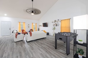 A modern living room with a sofa set, a foosball table, and a TV mounted on the wall. - Kitchen Foosball Fenced Yard Parking (Kyle)
