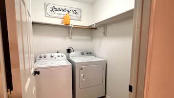 A laundry room with two washers and a dryer, a sign above the dryers, and a small shelf with a cup.