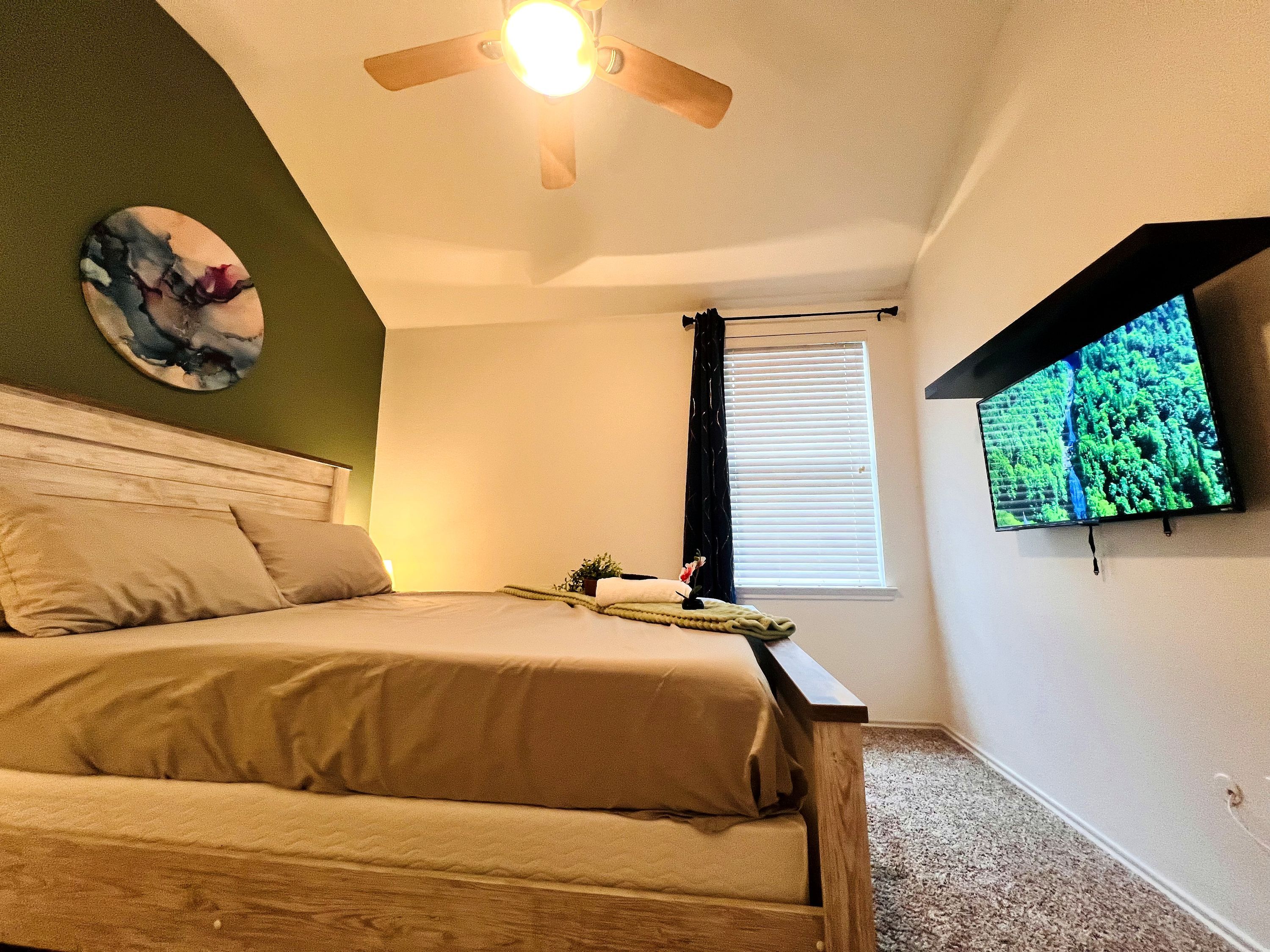 Een slaapkamer met een bed, een plafondventilator, een tv aan de muur en een raam met zonwering.