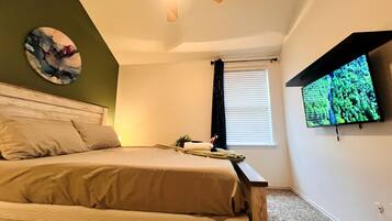 Een slaapkamer met een bed, een plafondventilator, een tv aan de muur en een raam met zonwering.