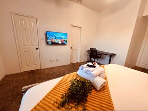 Habitació d'hotel amb un llit, un televisor a la paret, escriptori amb cadira i una planta damunt el llit.