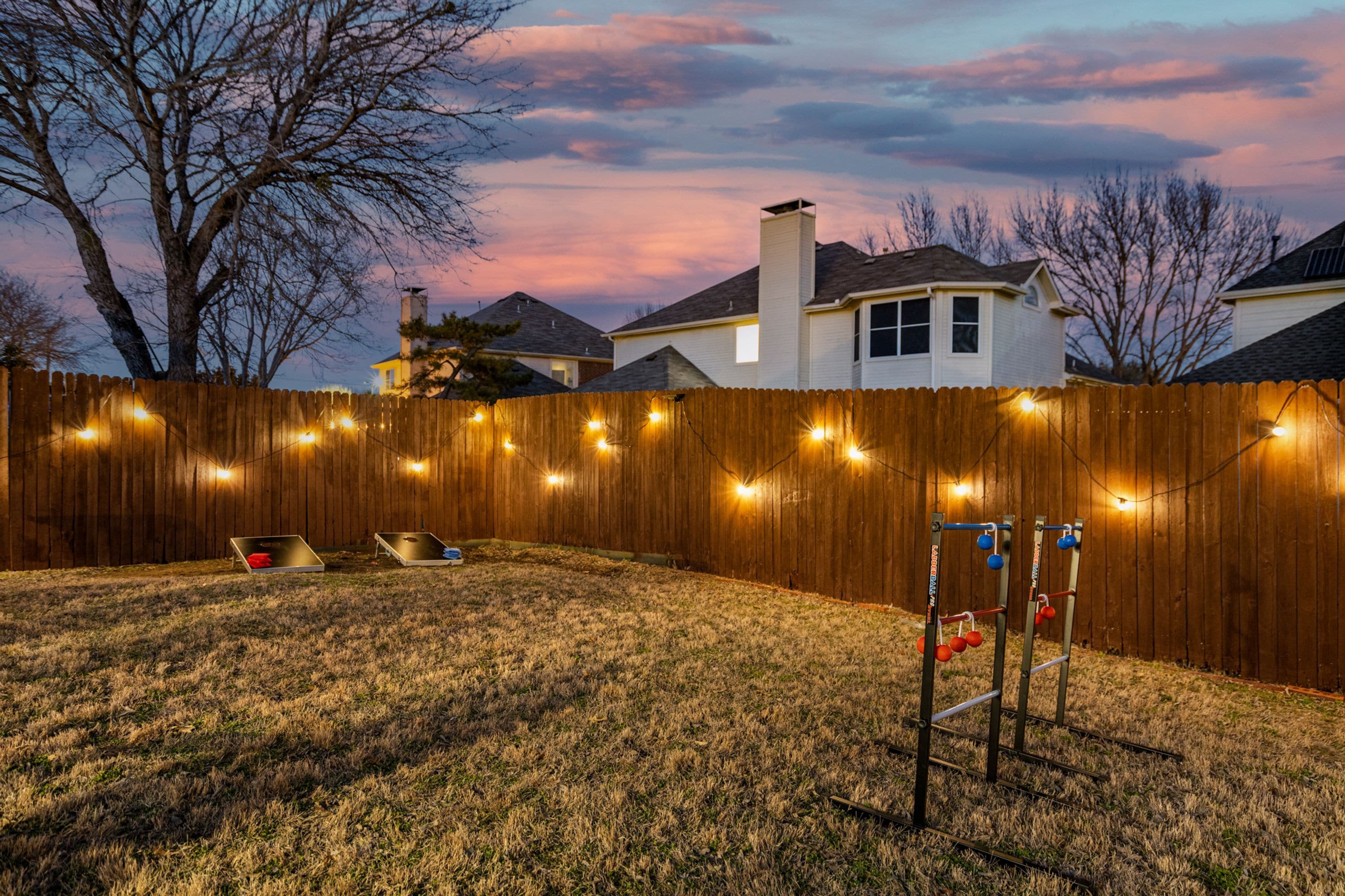 A backyard with a wooden fence, string lights, and a metal play structure.