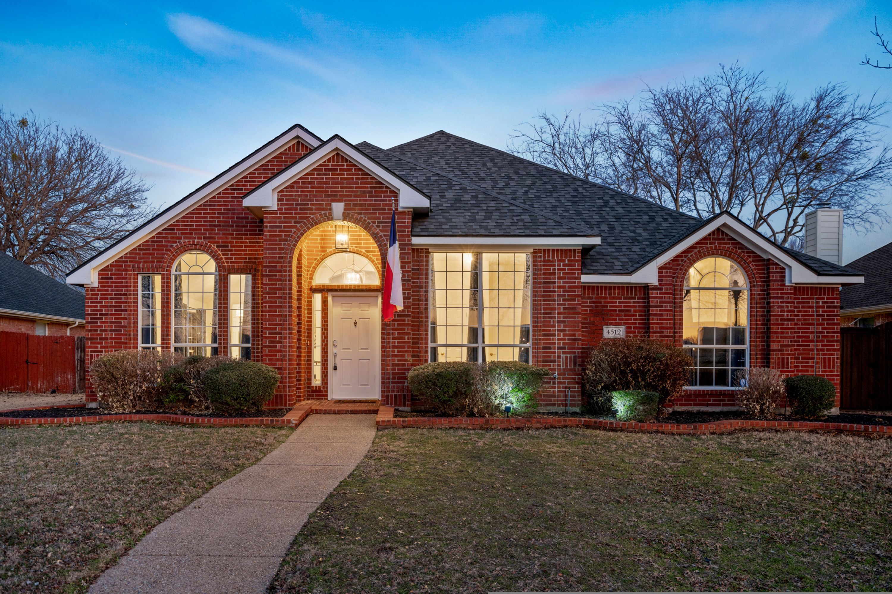 A two-story brick house with a central entrance, large windows, and a well-maintained lawn.
