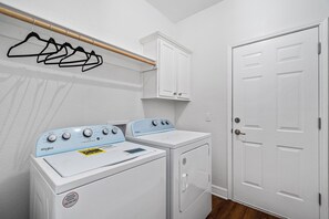 Un lavadero con lavadora y secadora Whirlpool, un tendedero de madera y una puerta blanca.