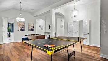 Una habitació àmplia amb taula de ping-pong, taula de futbolí i ventilador de sostre.