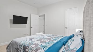 A bedroom with a bed, a television mounted on the wall, and two doors.