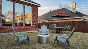 A backyard with a fire pit, two Adirondack chairs, a table, and a red umbrella.