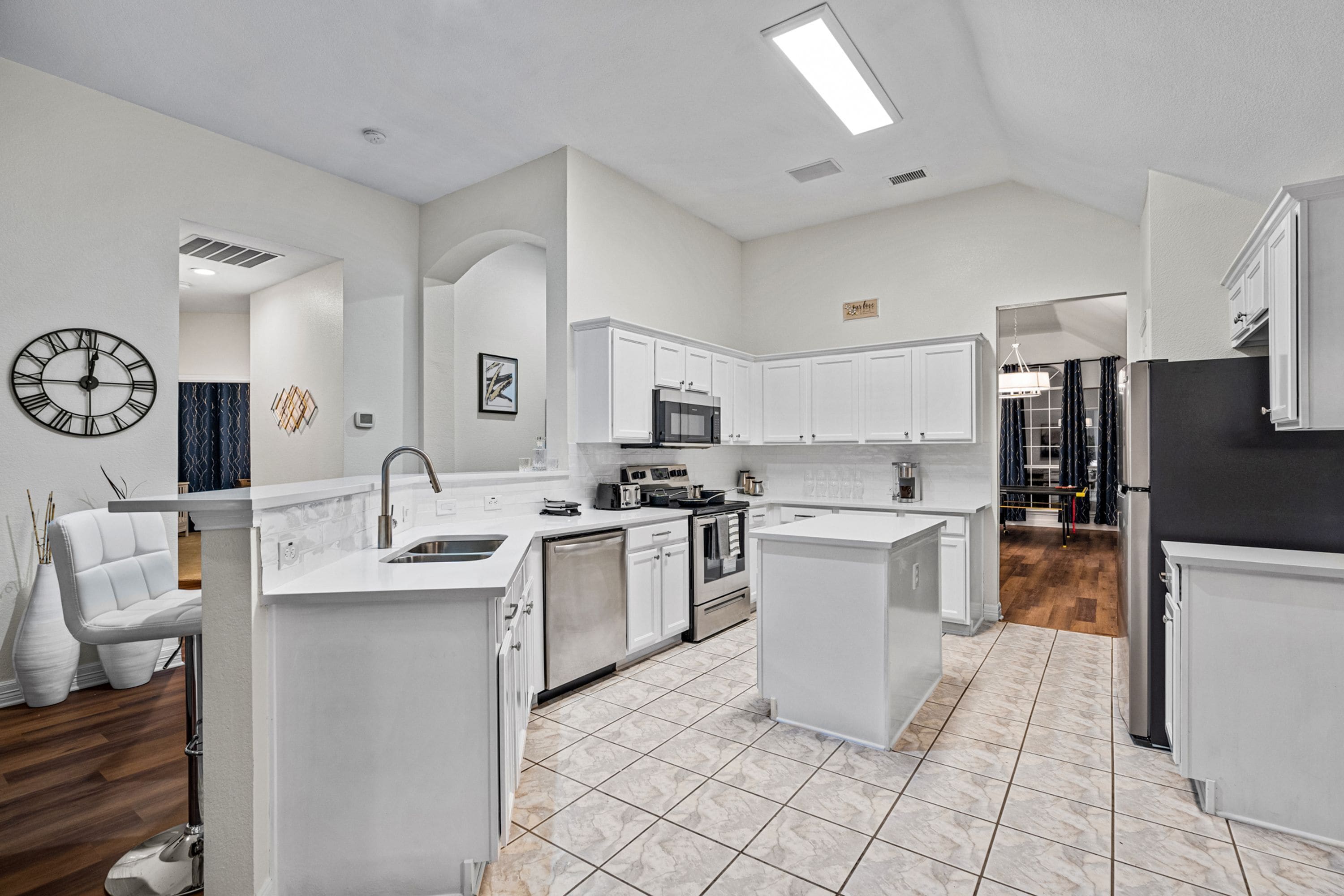 A modern kitchen with white cabinetry, a stainless steel sink, and a tiled floor.