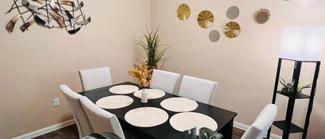A dining area with a black table, white chairs, and decorative wall art.