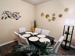 Un comedor con una mesa negra, sillas blancas y detalles decorativos en la pared.