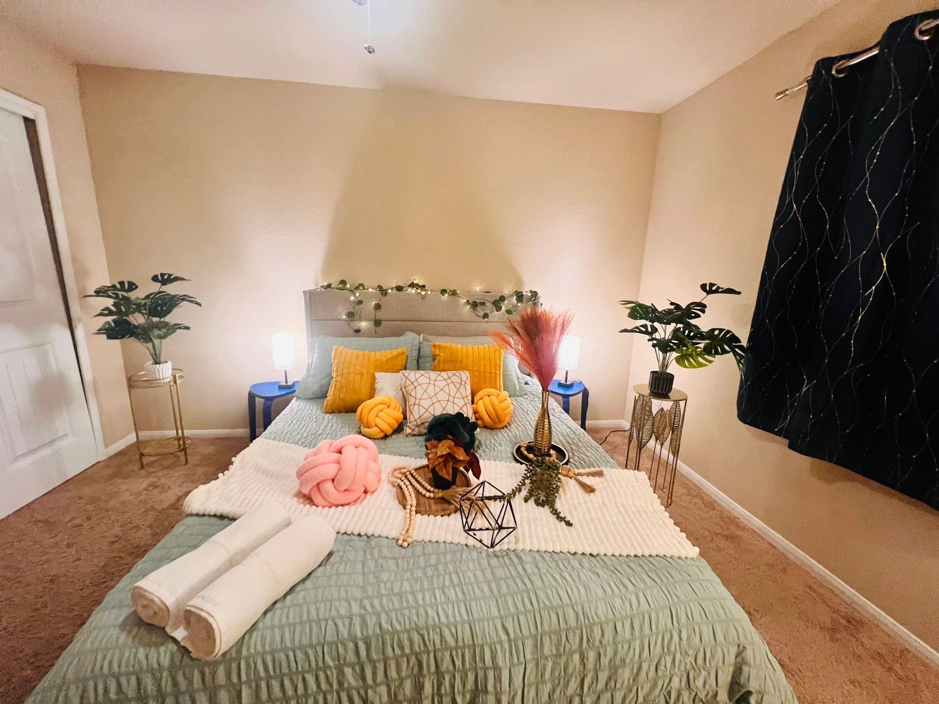 Une chambre à coucher avec un lit, des oreillers, une table de chevet, une lampe et une plante en pot.
